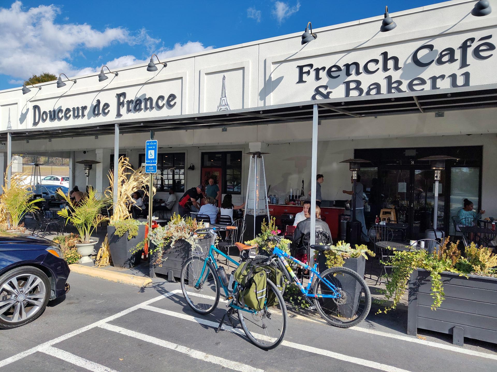 Two blue bicycles (one covered in stickers) parked in front of a patio where people are eating and drinking.