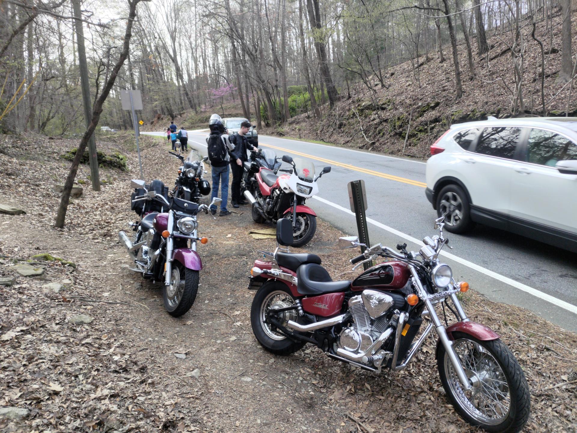 Several motorcycles pulled off onto the dirt between a trail and the road.