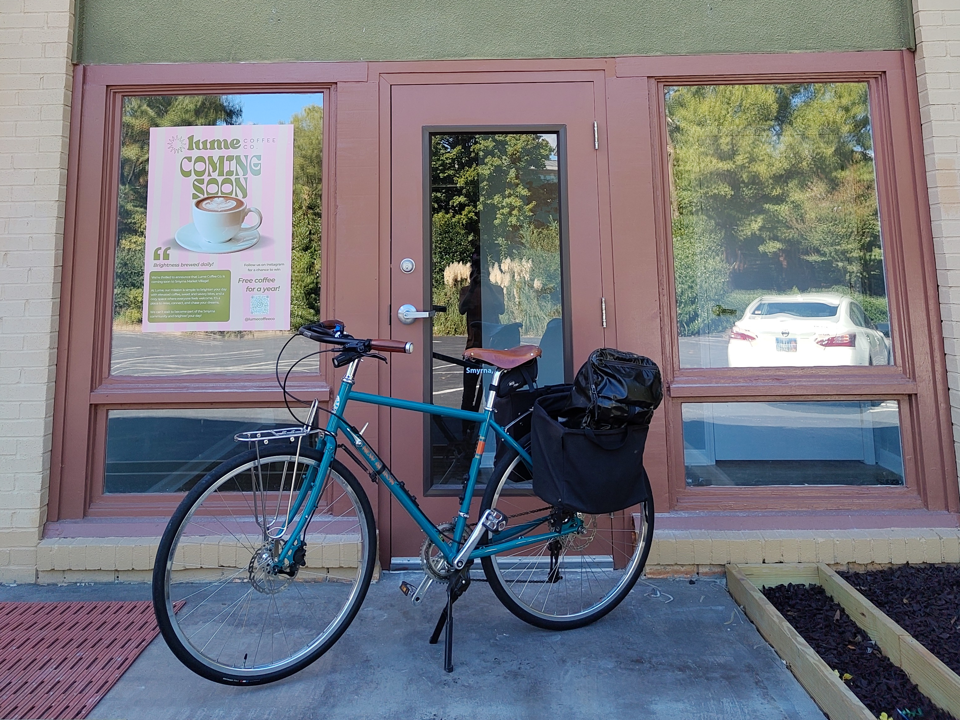 A blue bicycle parked in front of a shop front with a sign next to it that says Lume Coffee Co Coming Soon.